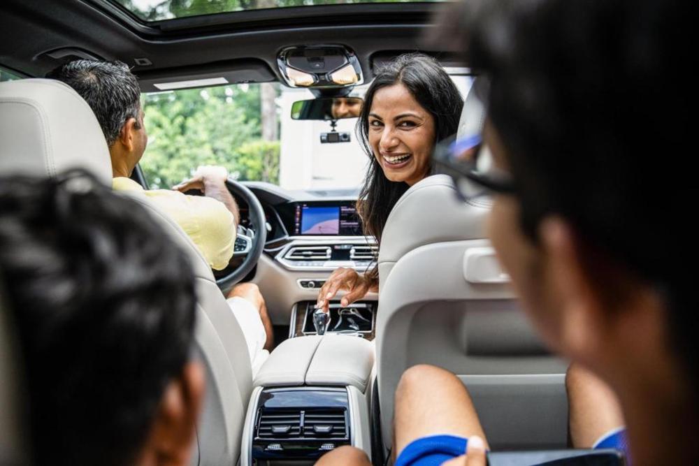 A woman sitting in the front seat of her car smiling lovingly at her children in the back seat