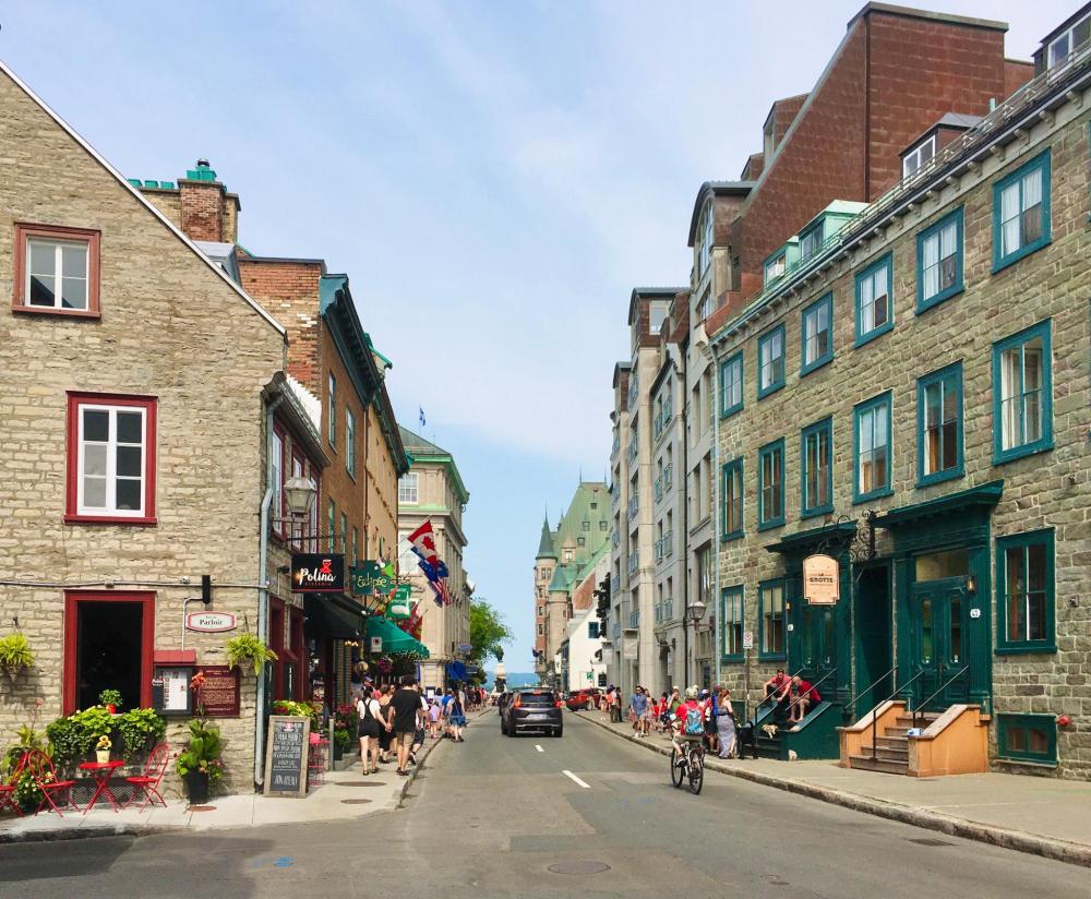 A view of Rue Saint-Louis in Old Quebec, featuring historic stone buildings, shops, and a view of the Château Frontenac in the distance.