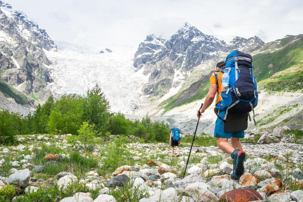Hikers walking through a rocky mountain valley beneath snow-covered peaks
