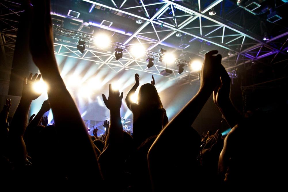 Concert crowd with raised hands under bright stage lights.