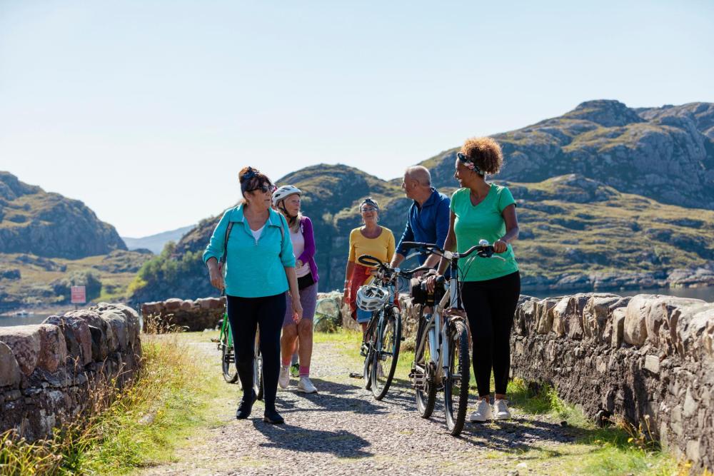 Group of adults walking and cycling along a path through a mountainous landscape.