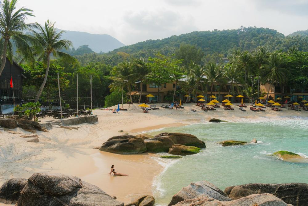 Sandy beach with palm trees, sun loungers and tropical hills in Thailand