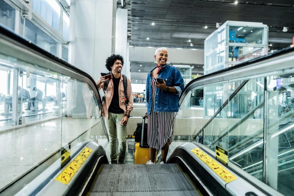 Two people standing side by side on an airport escalator, with luggage beside them as they ascend.