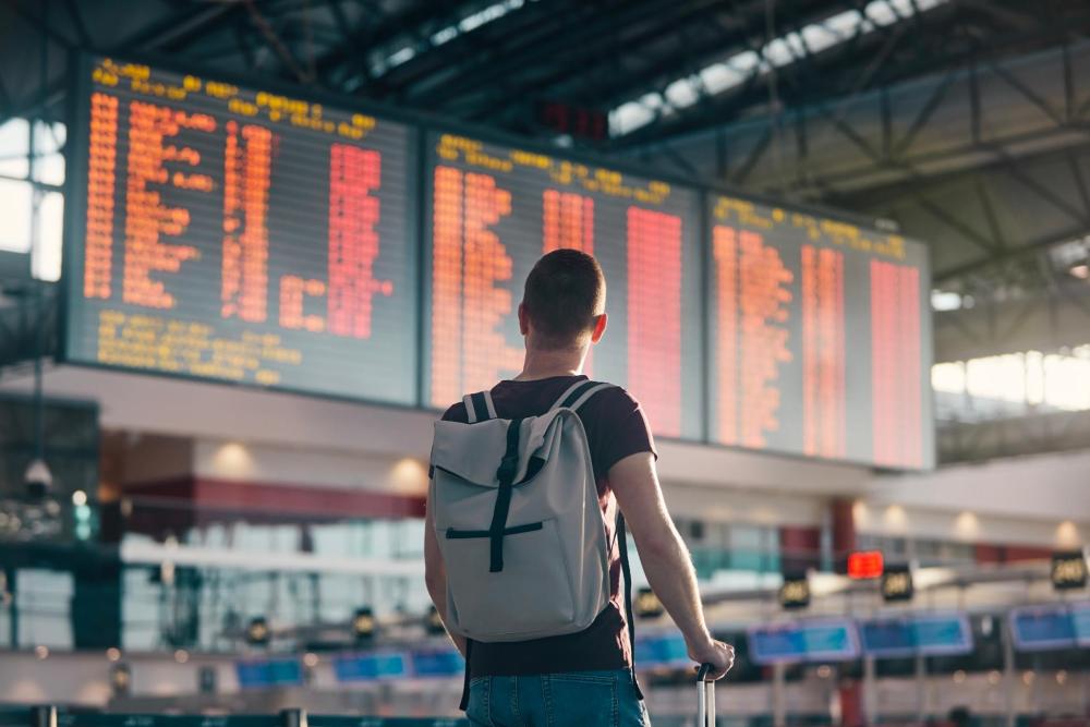 空港でフライトスケジュールをチェックし旅行に出かける男性