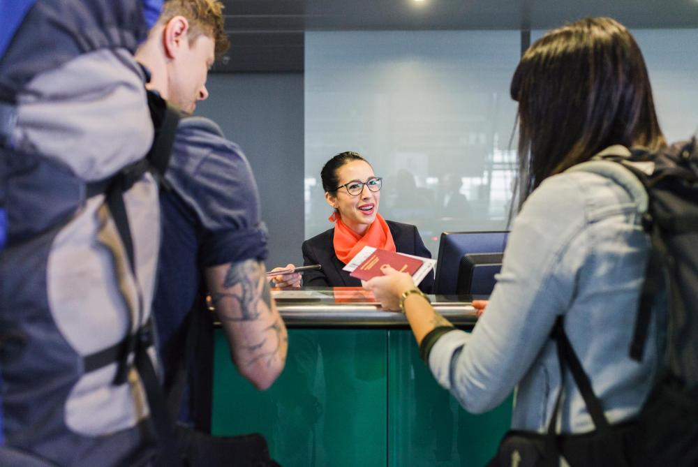 Two travelers hand over a passport at a reception desk while a staff member assists them during hotel check-in