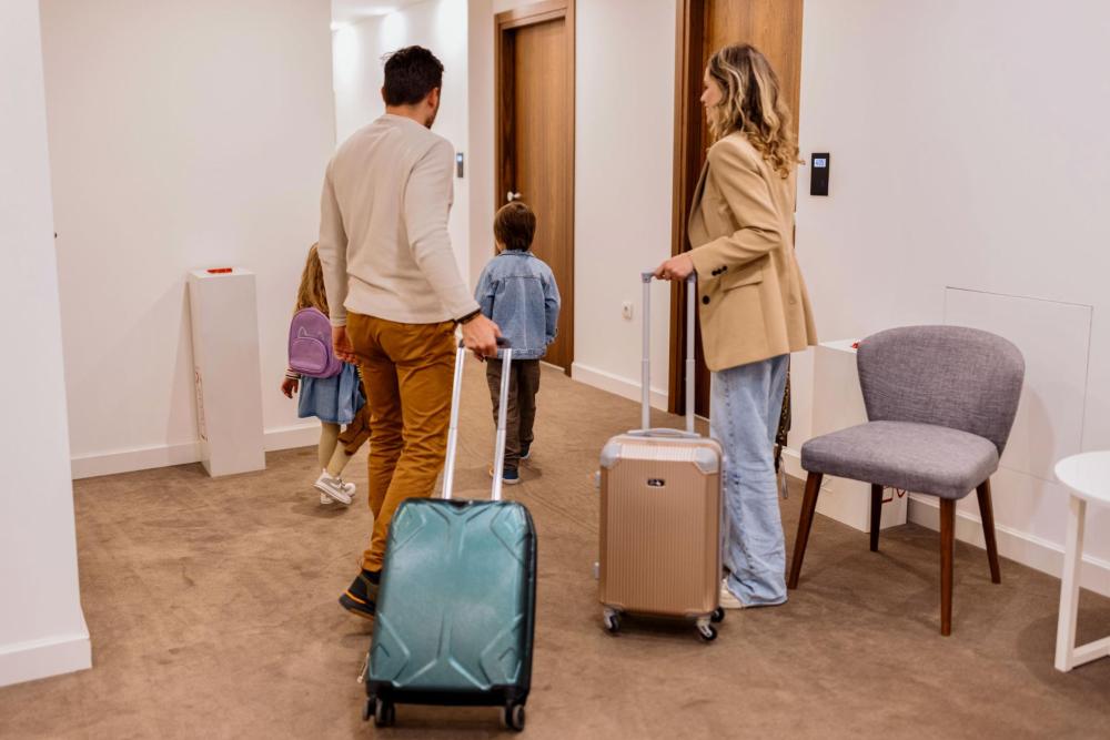A man, woman, and two children carrying luggage entering a hotel room