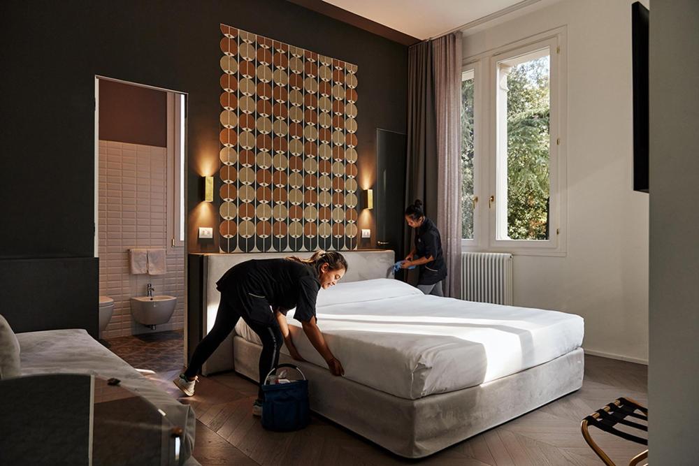 Two hotel staff members clean and organize a bed in a hotel room