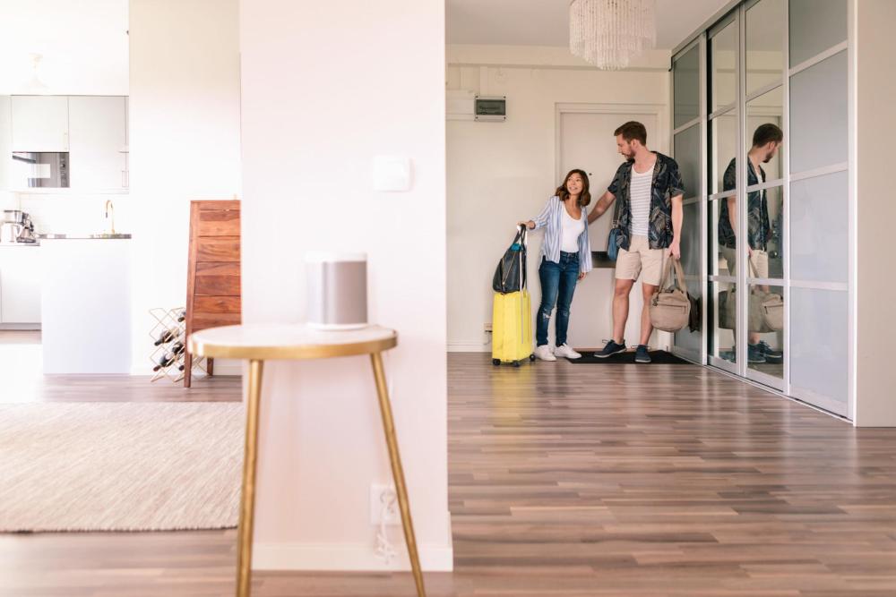 A man and woman carrying bags and a suitcase enter an apartment together.