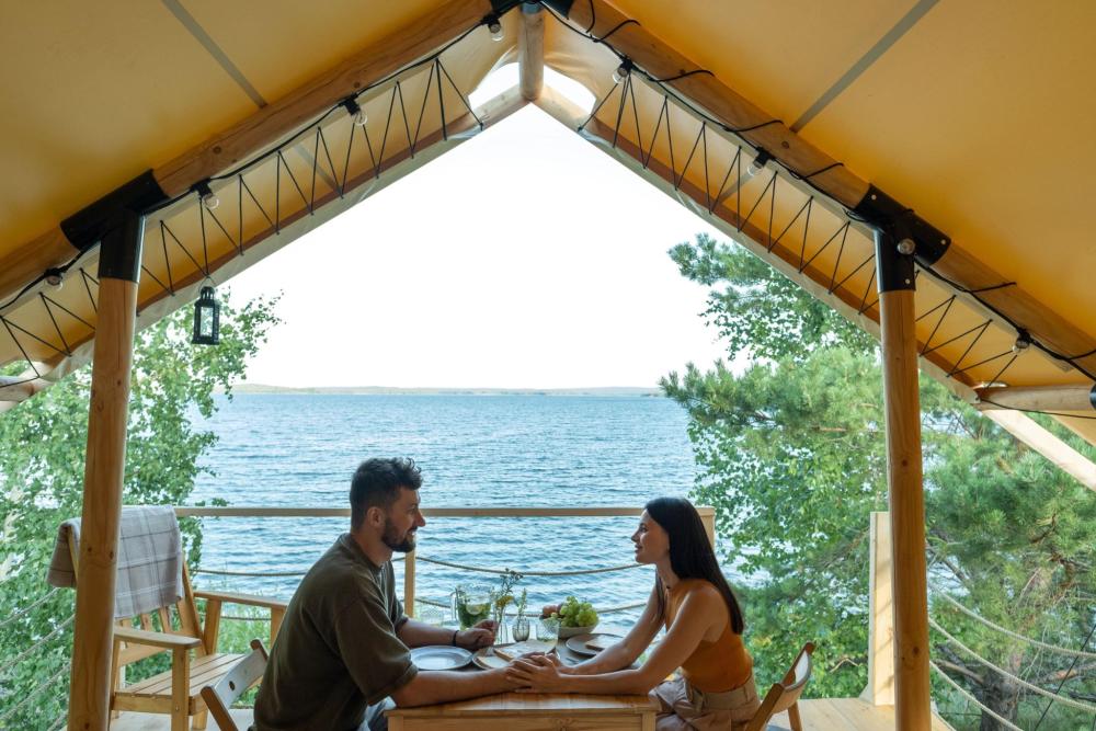 Couple sharing a meal inside a glamping tent overlooking a lake