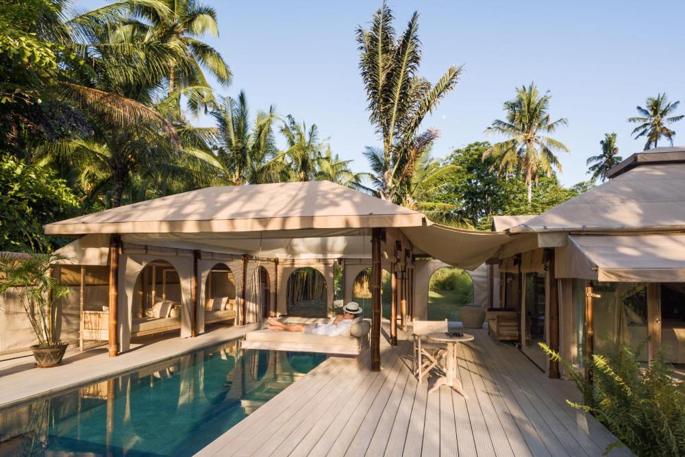 High-end glamping tent with a swimming pool and a man laying on a swinging bed above it