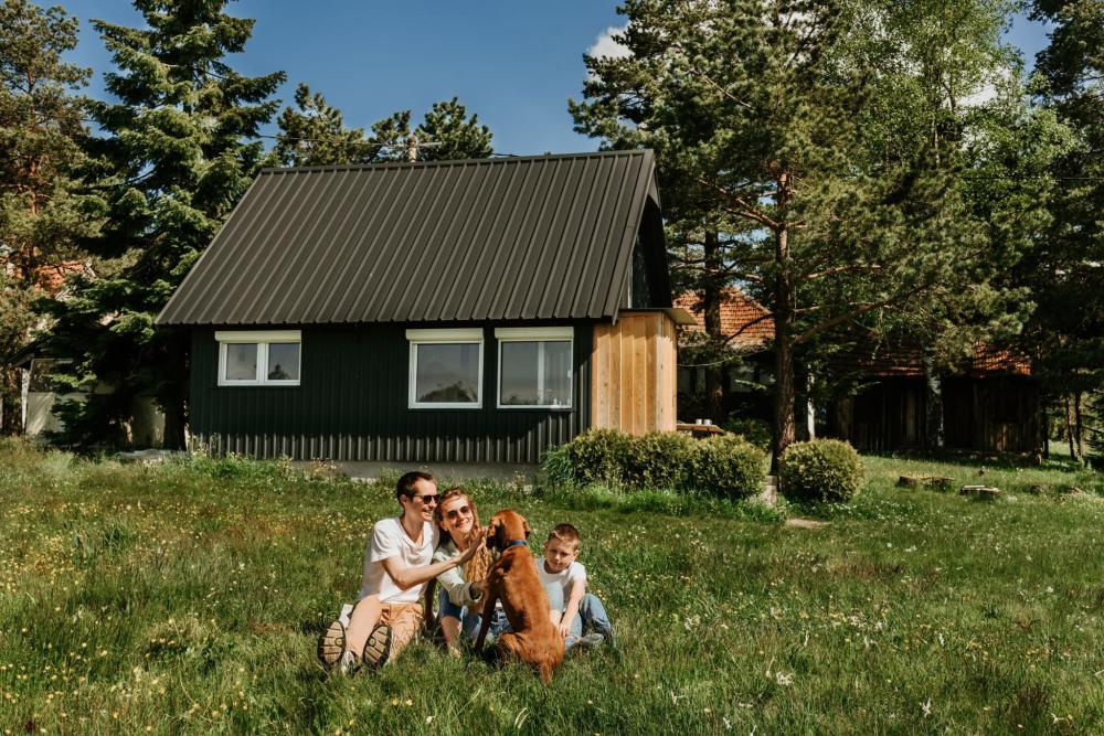 Family sitting on the grass with a dog outside a cabin surrounded by trees