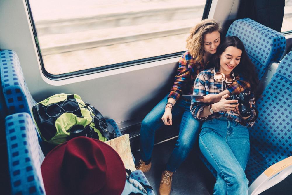 Two people on a train looking towards the camera with backpacks beside them