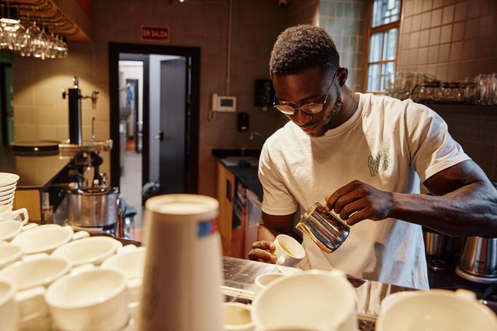A staff member serves coffee by pouring it into cups for a customer