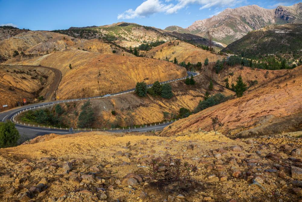 Panoramic view of a mountain road winding through eroded, golden-brown hills in Tasmania