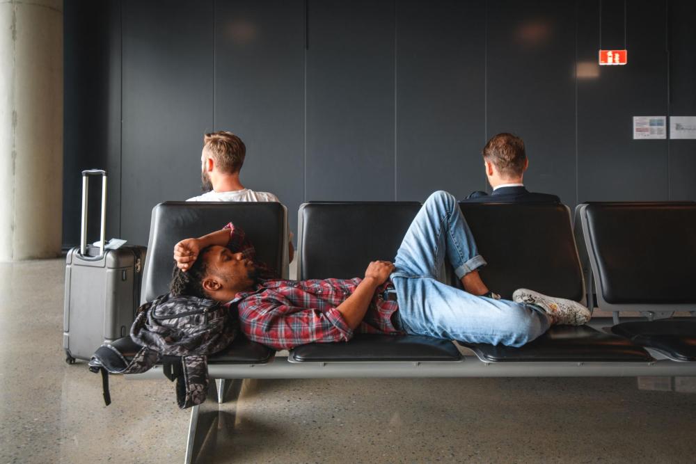Traveller lying across airport seats with luggage nearby while waiting in the terminal