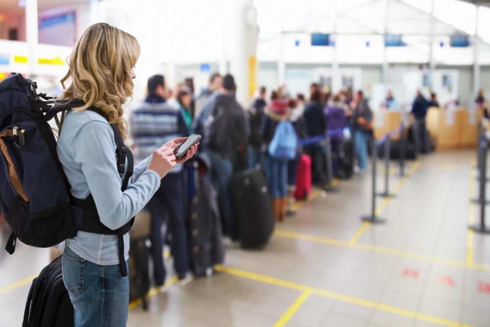 Traveller with a backpack checks a phone while standing in a queue at the airport