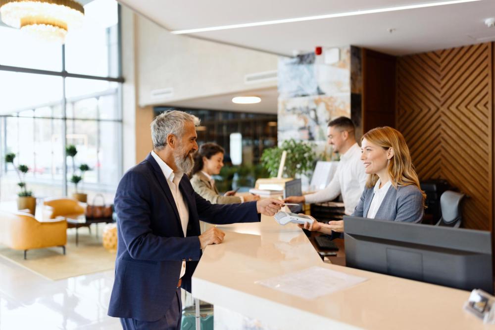 A business traveler checks in at a hotel front desk while speaking with a staff member.