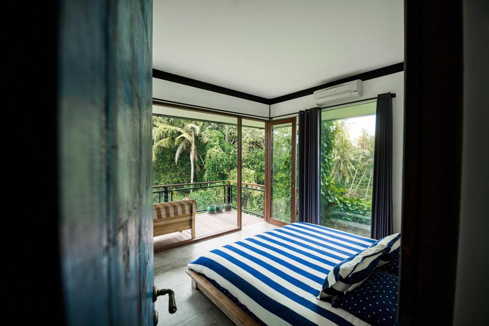 Bedroom with a striped bed, floor-to-ceiling windows and a balcony overlooking lush tropical greenery