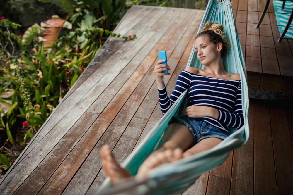 A woman relaxes outdoors in a hammock while looking at her smartphone
