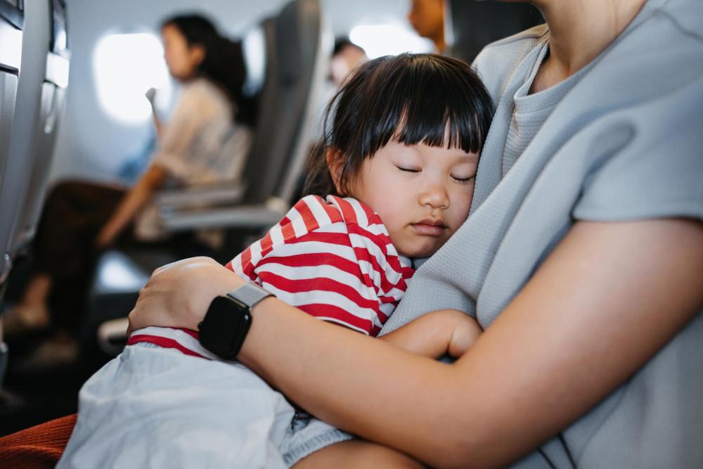 機内で大人の膝に座り眠る子ども