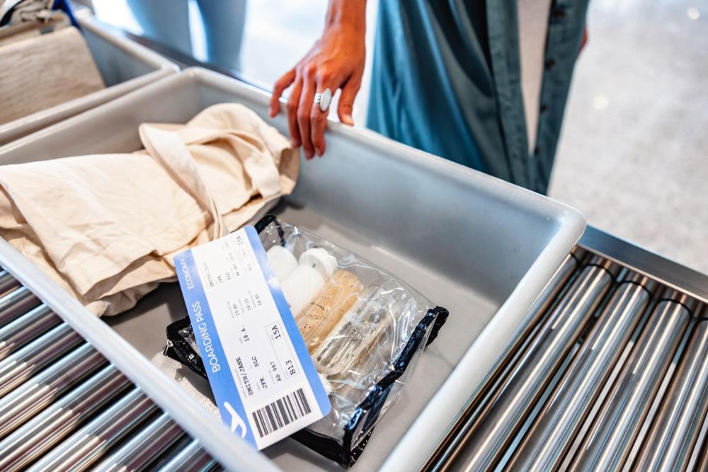 Bac de contrôle contenant un tote bag, une carte d’embarquement et un sac transparent contenant des produits liquides posés sur un tapis roulant d'aéroport