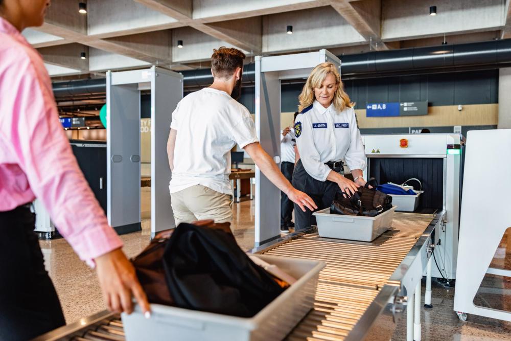Une agente de sécurité supervise le contrôle des bagages de passagers sur un tapis roulant à l’aéroport