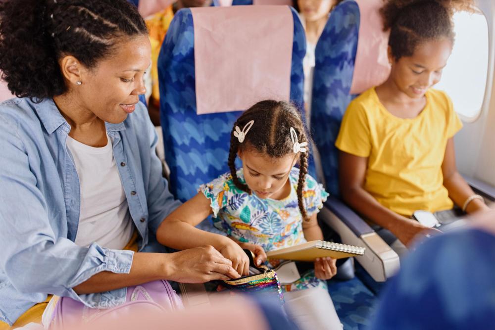 A mother helps her kid with craft supplies while flying on an airplane