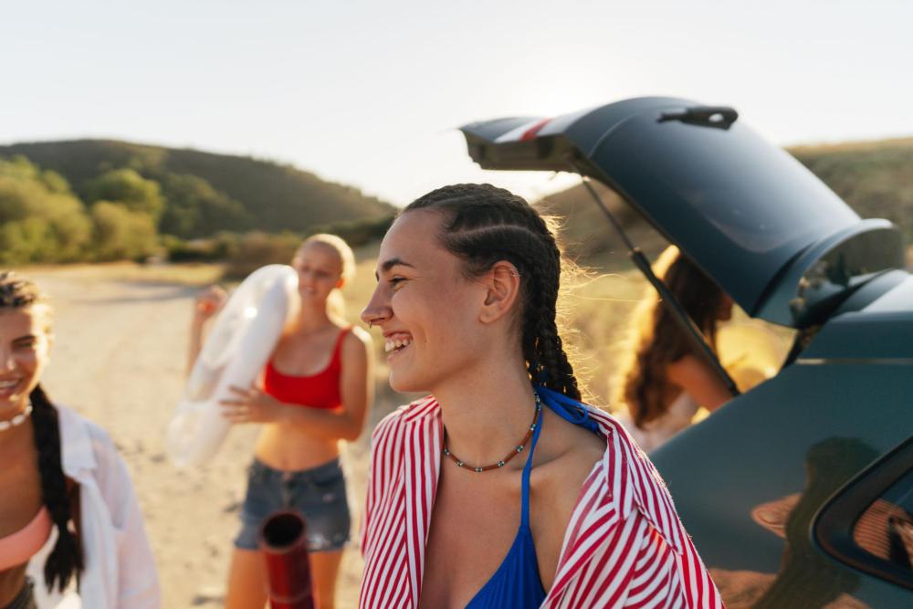 A group of friends smiling and unpacking a car on a sunny day at the beach