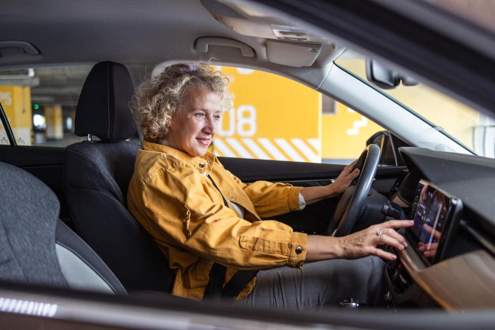 A woman using a touchscreen display while sitting in the driver’s seat of a car