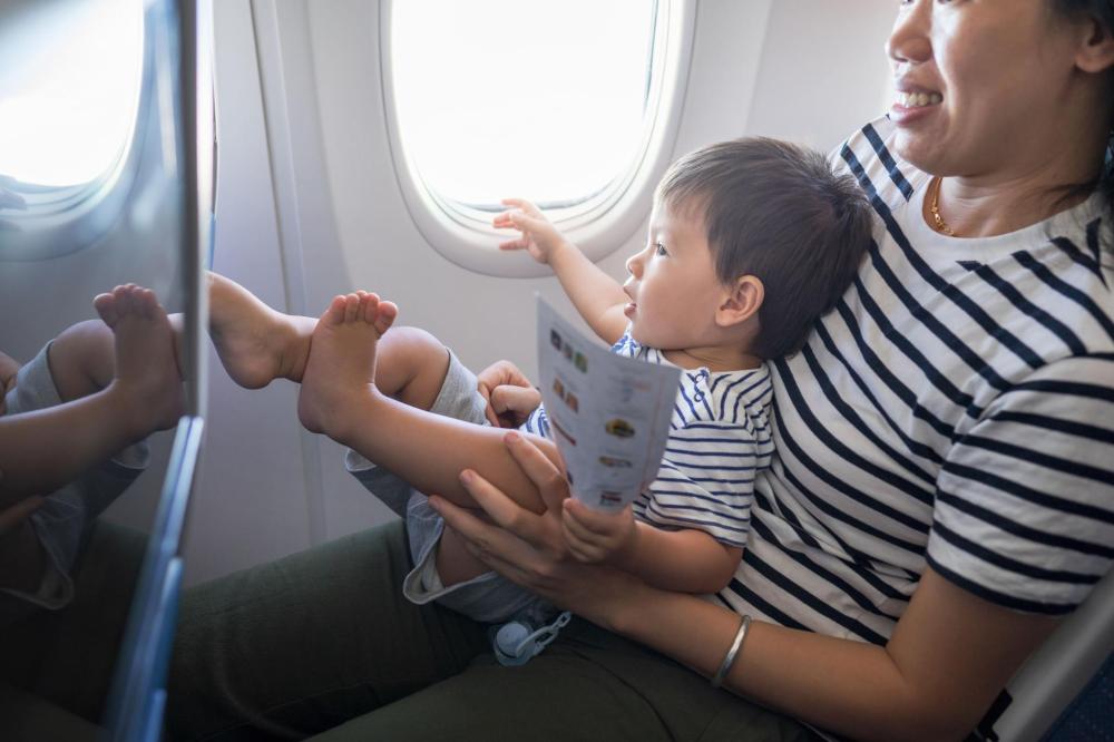 A young boy sitting on a woman's lap during a flight and pointing toward the window