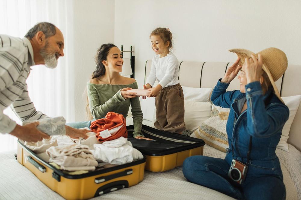 Une famille est assise sur un lit, remplissant une valise de vêtements