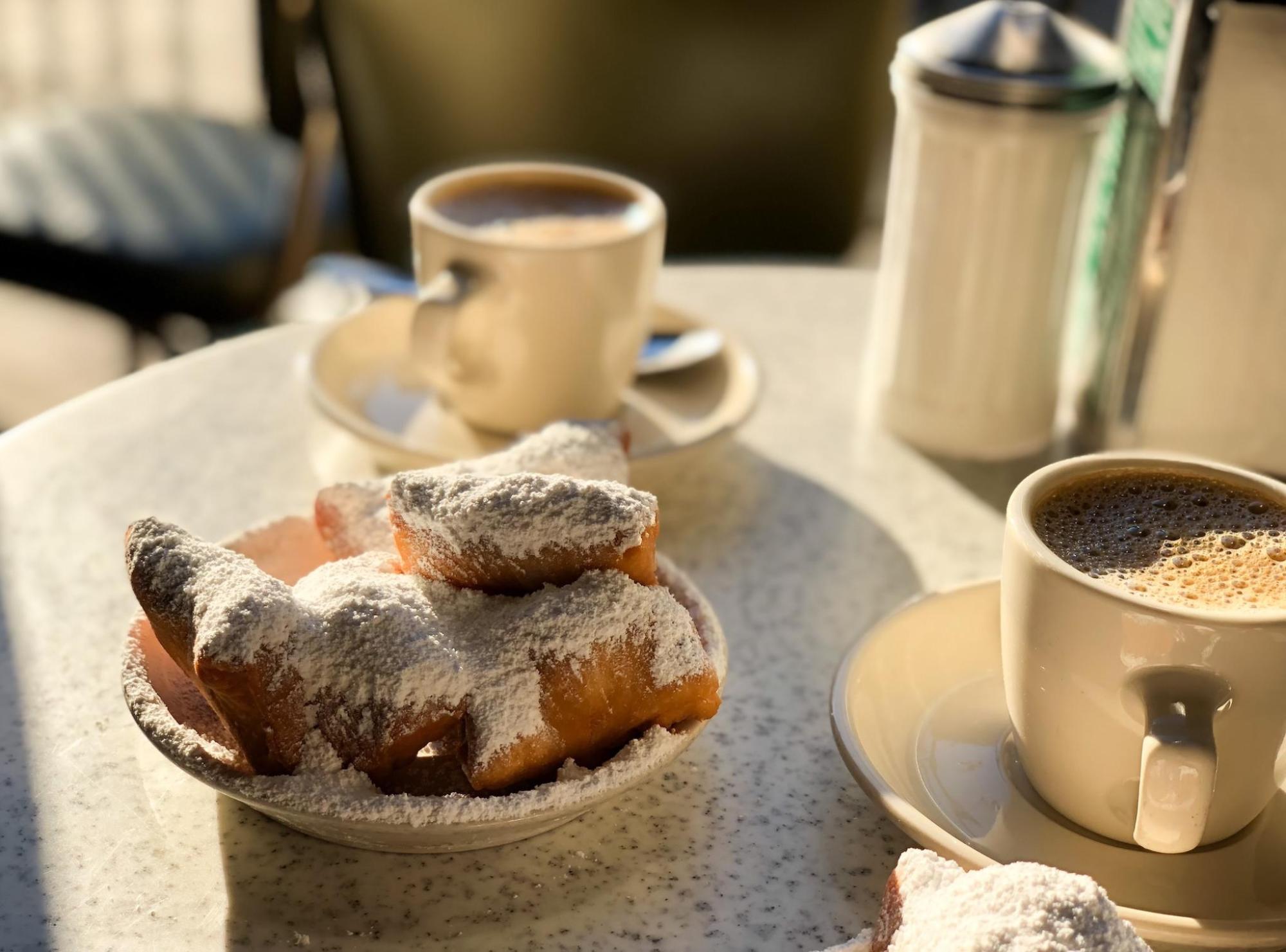 Two cups of coffee beside a plate of beignets