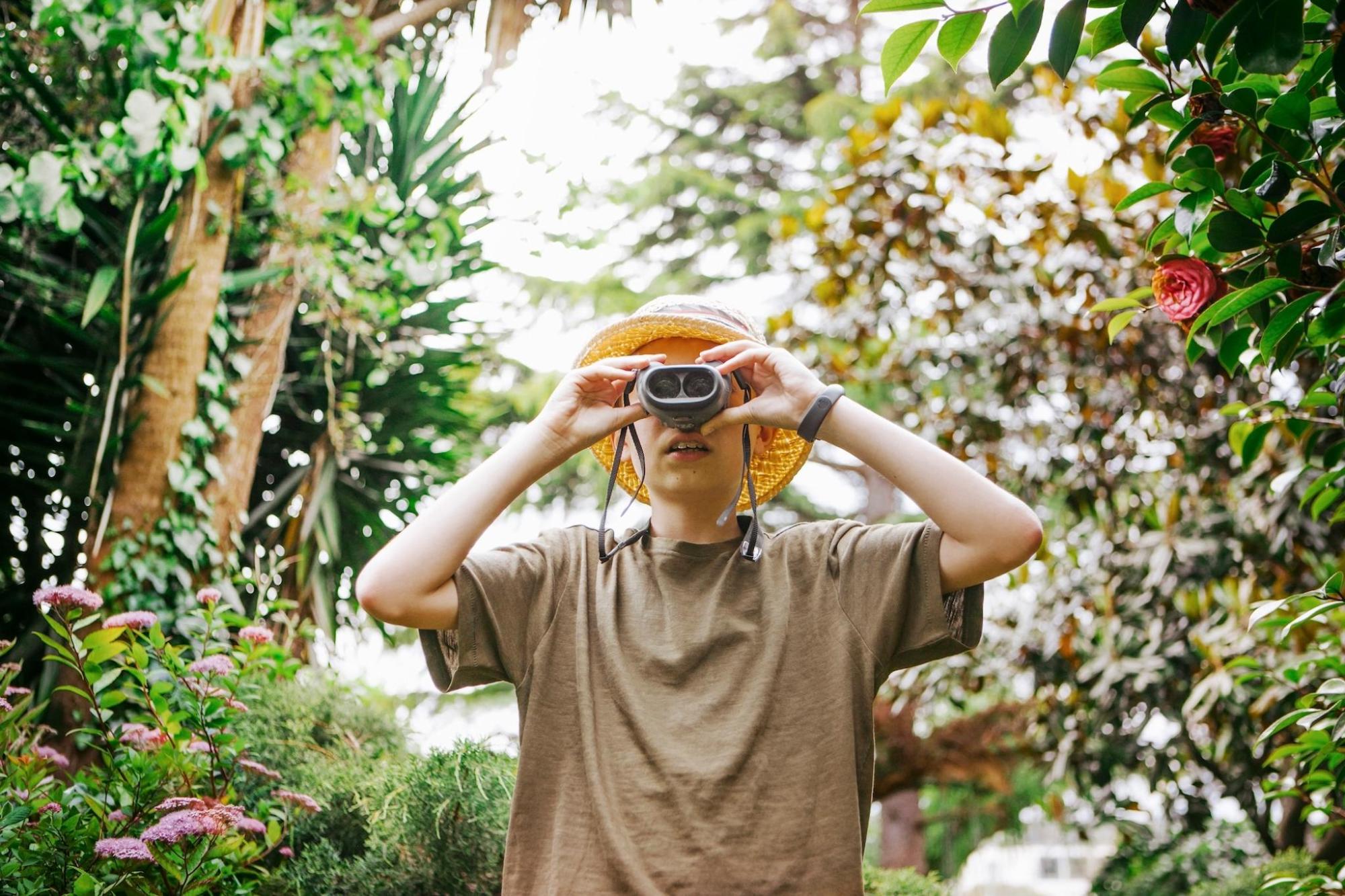 A boy in a hat holds binoculars, ready to observe wildlife
