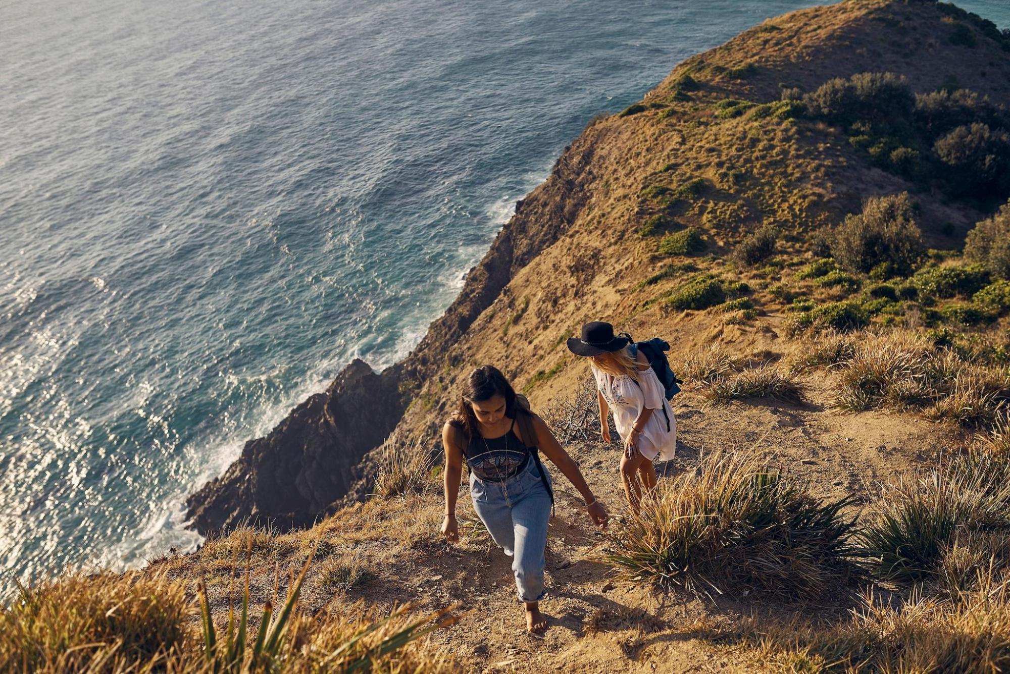 2 women hike on a hill with a view of the ocean in Australia