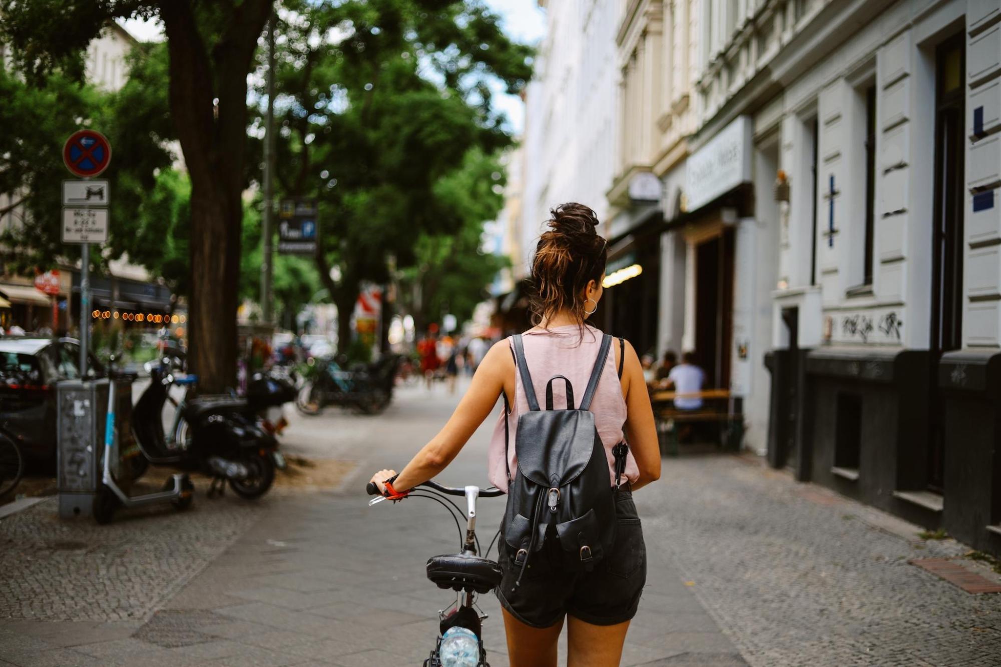 A woman with a backpack holds a bike on a street in Germany