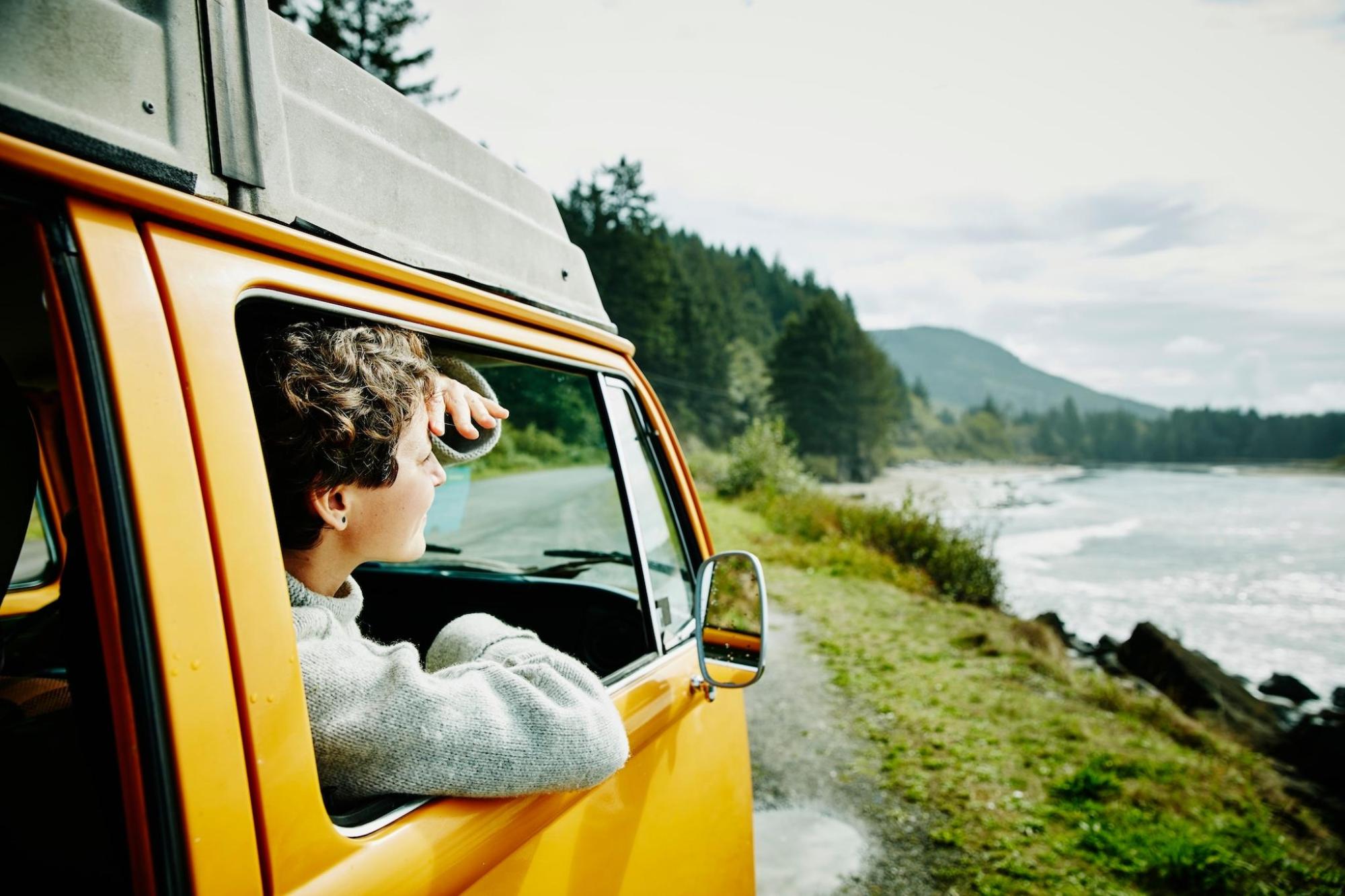 A smiling woman in the passenger seat of a parked yellow van