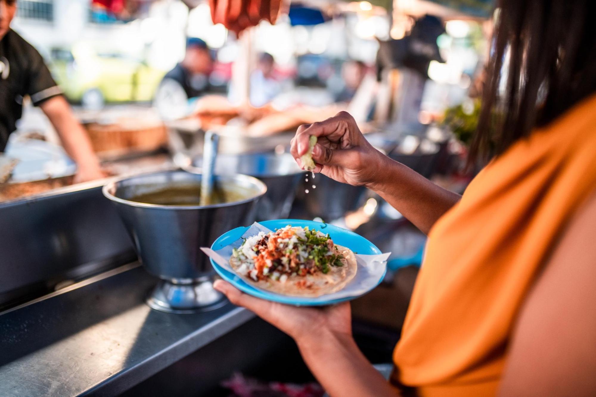 Una mujer echa lima a un plato de tacos que sujeta