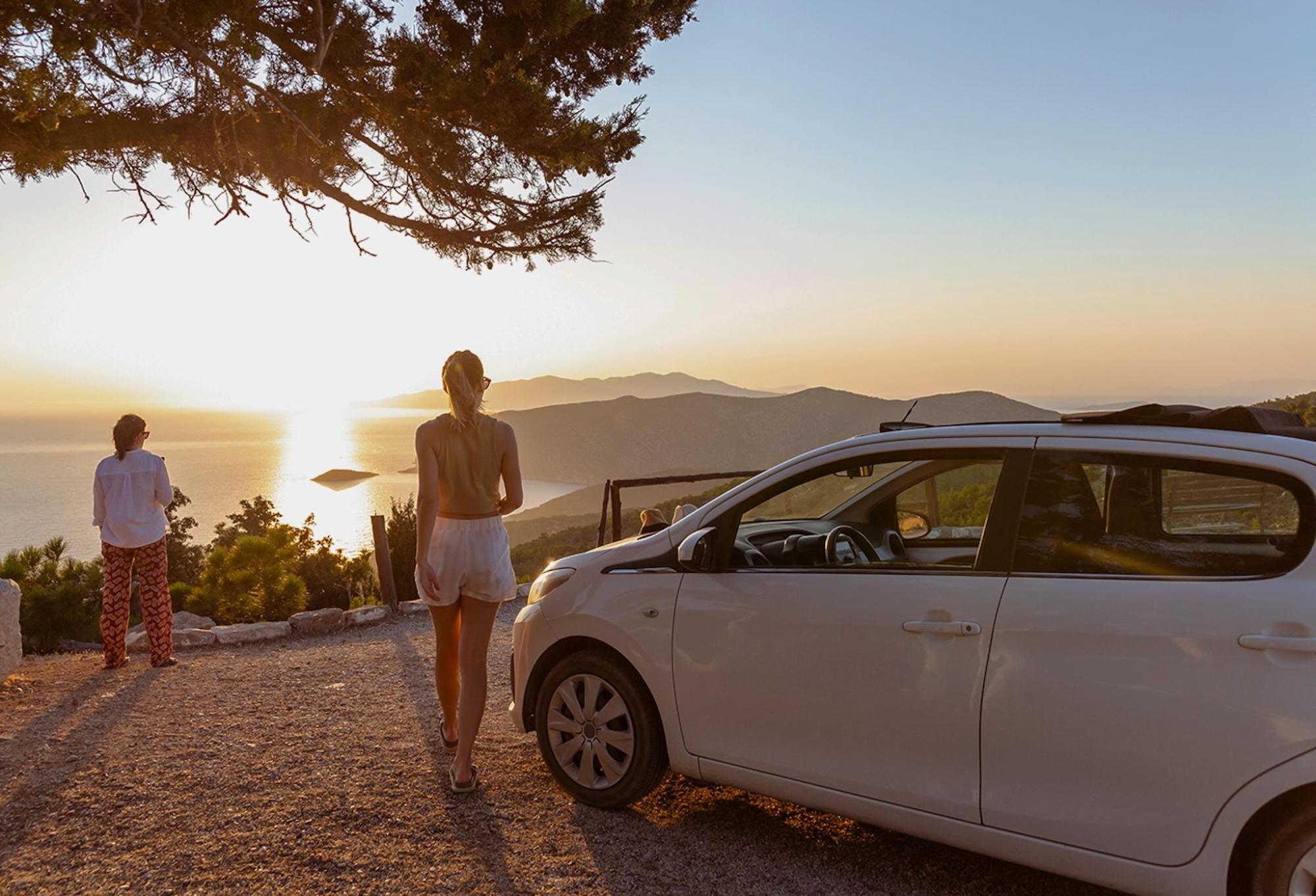 Two people stand beside a car, silhouetted against a sunset