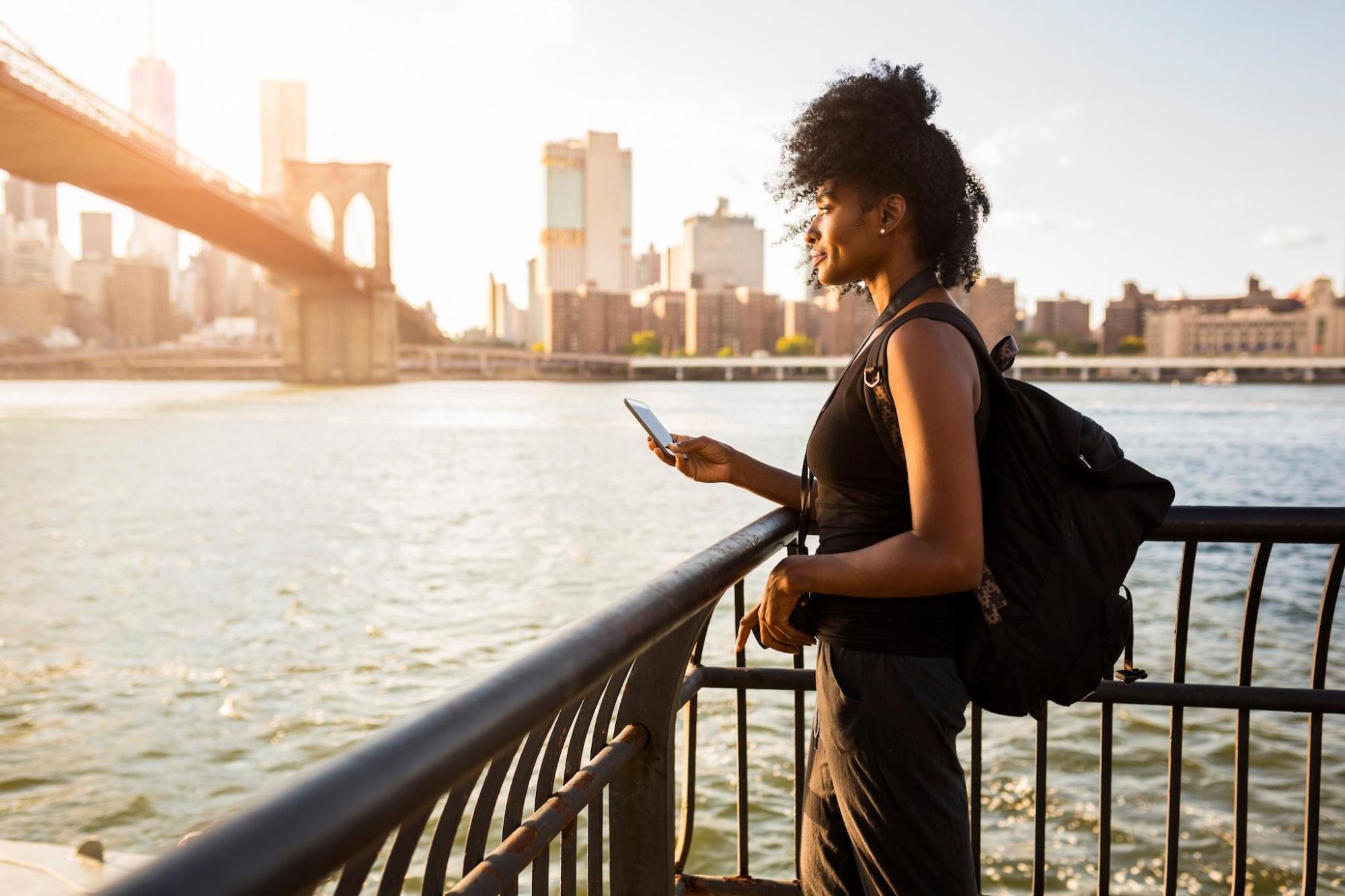 A woman holding a phone looking at NYC's landscapes