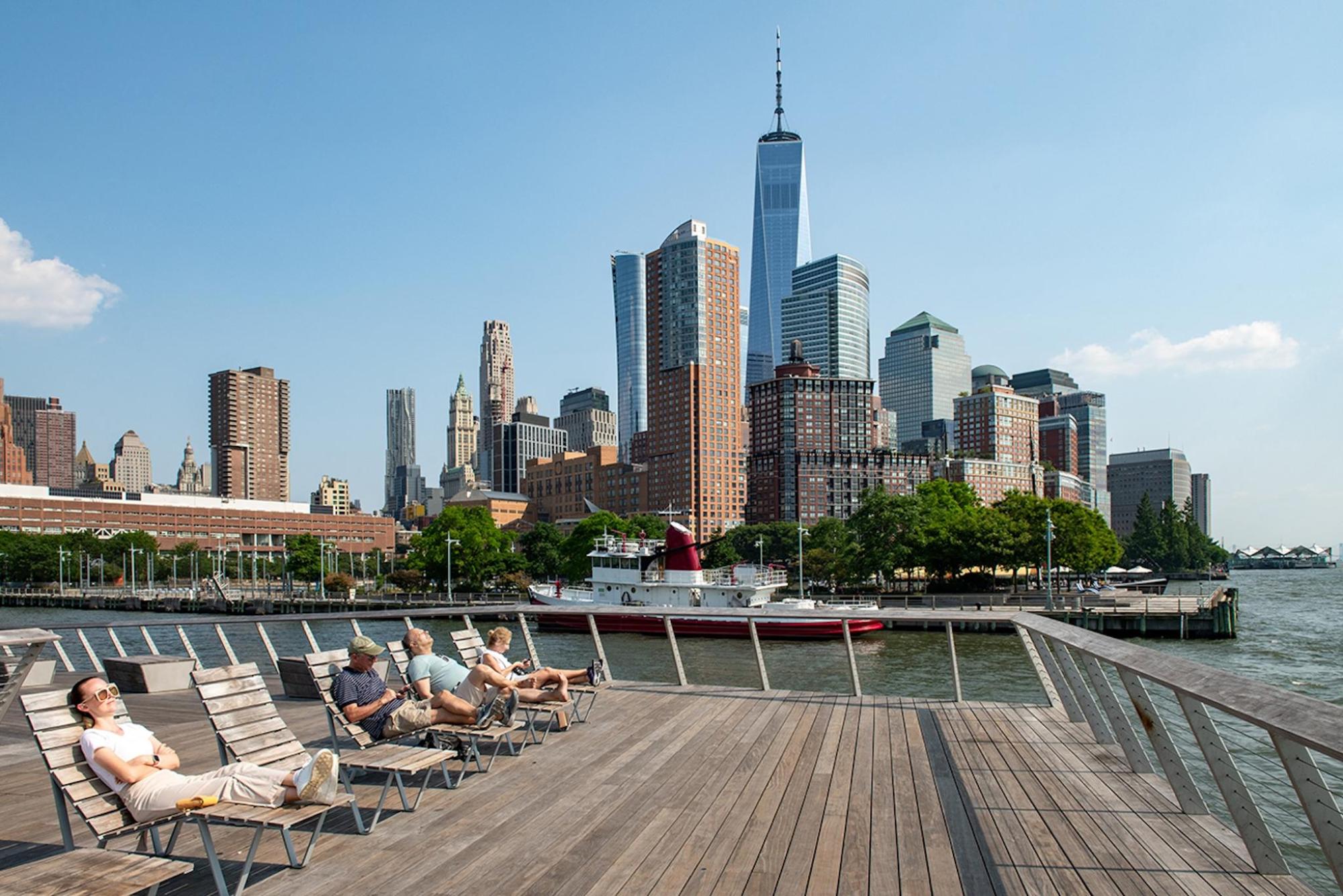 Individuals seated on a wooden deck next to NYC's skyline
