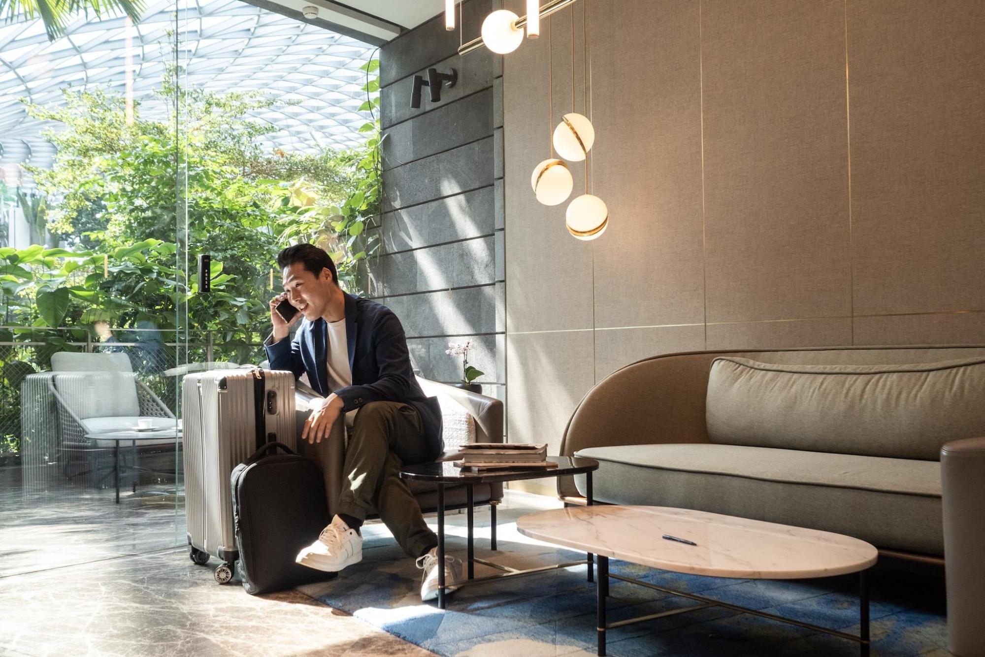 A man sat at a coffee table on the phone. He has a suitcase