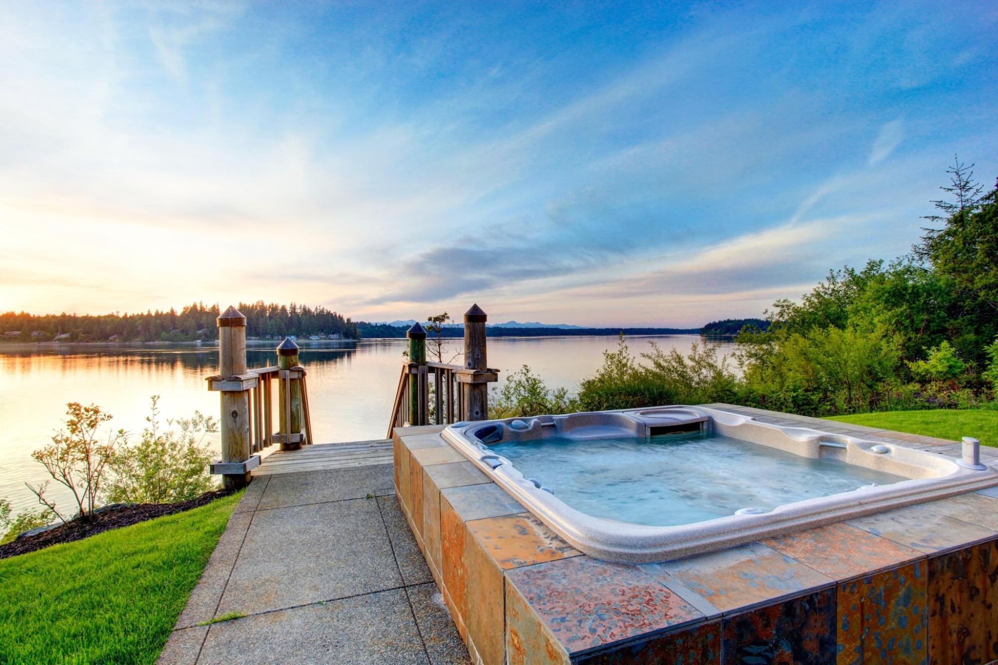 A cozy hot tub is positioned on a deck with a lake behind