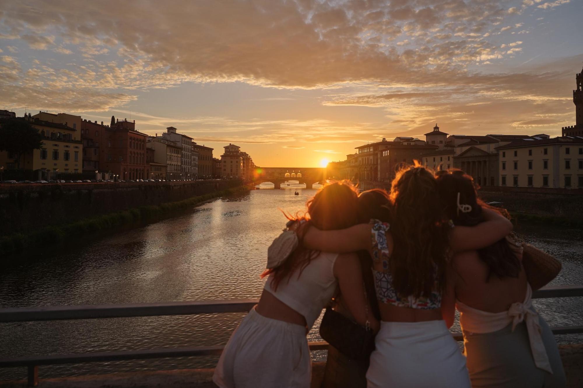 Four women stand on a bridge, gazing at a river in Florence