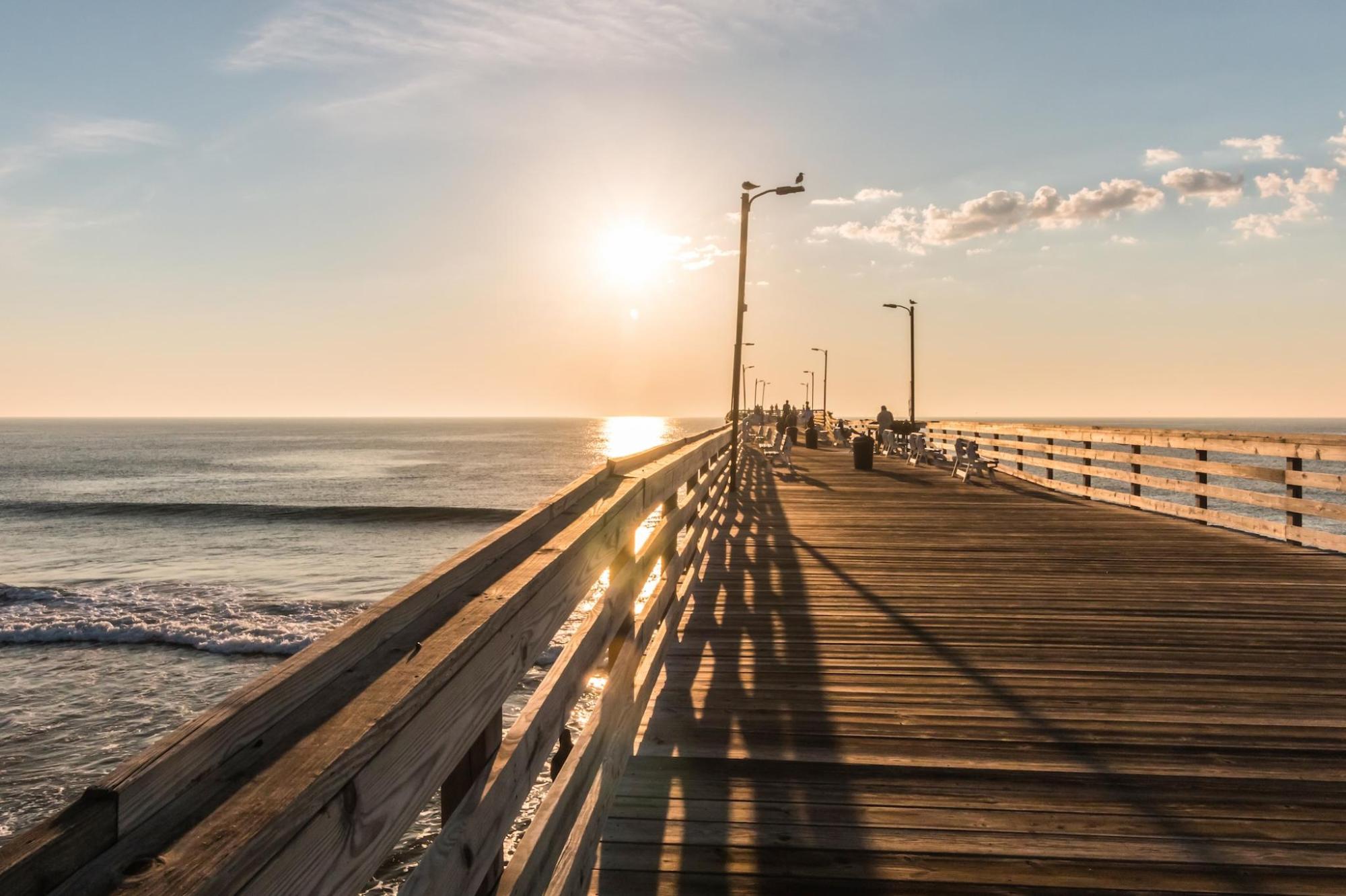 People stroll on Virginia Beach pier during a vibrant sunset