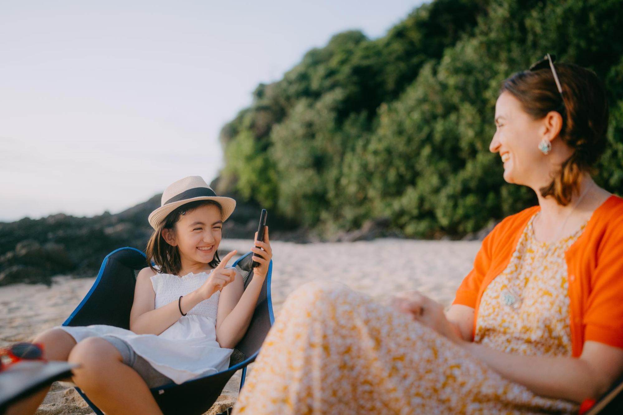 Young girl taking photo of her mother with phone on beach