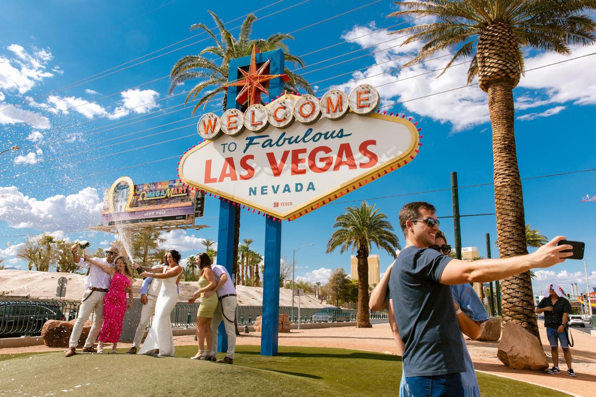A group smiles, taking photos at Las Vegas welcome sign