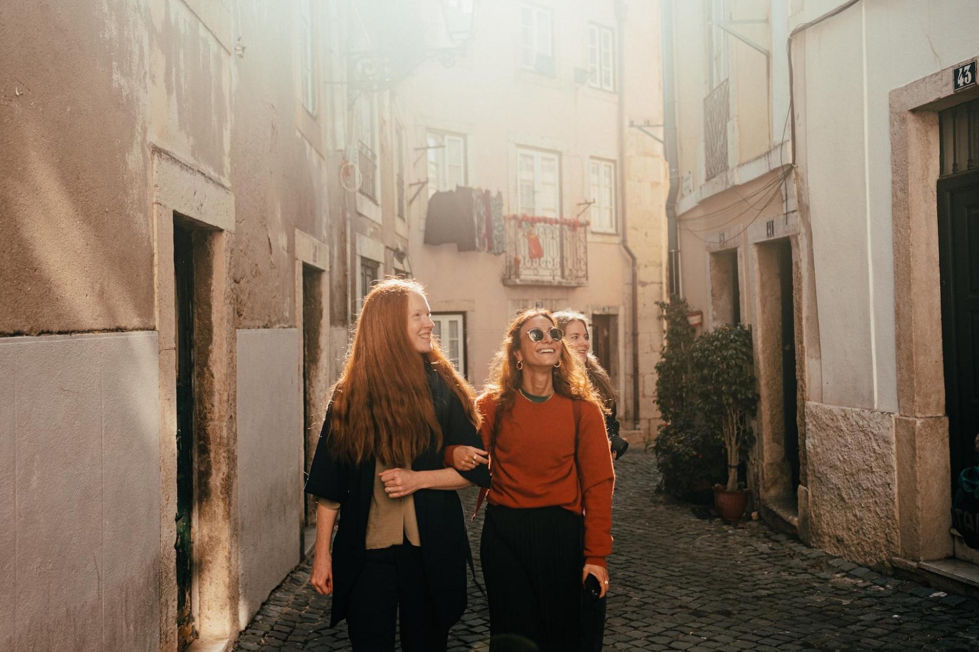 Three women walking together down a narrow alley in Lisbon