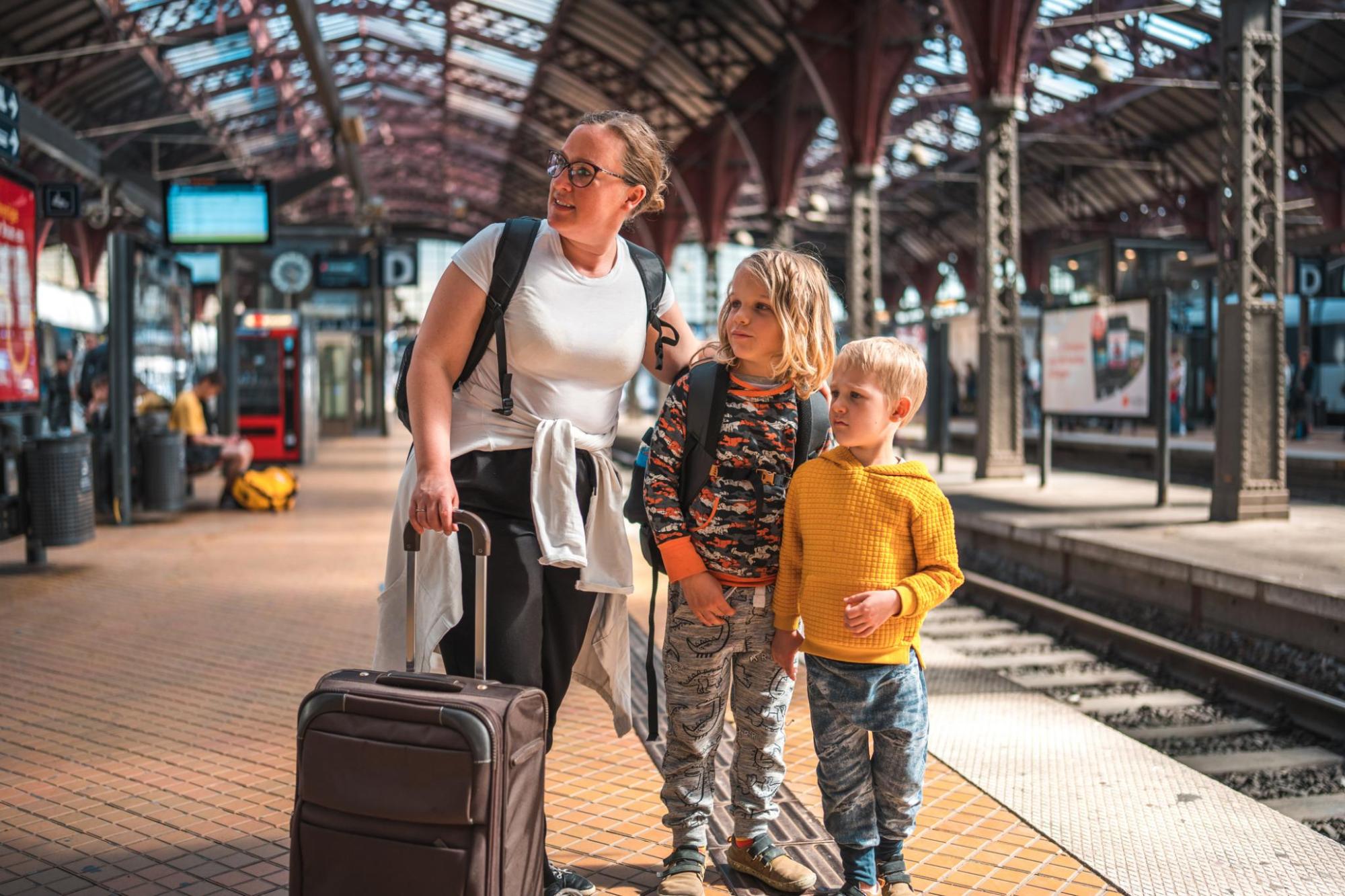 A woman standing with two children carrying luggage