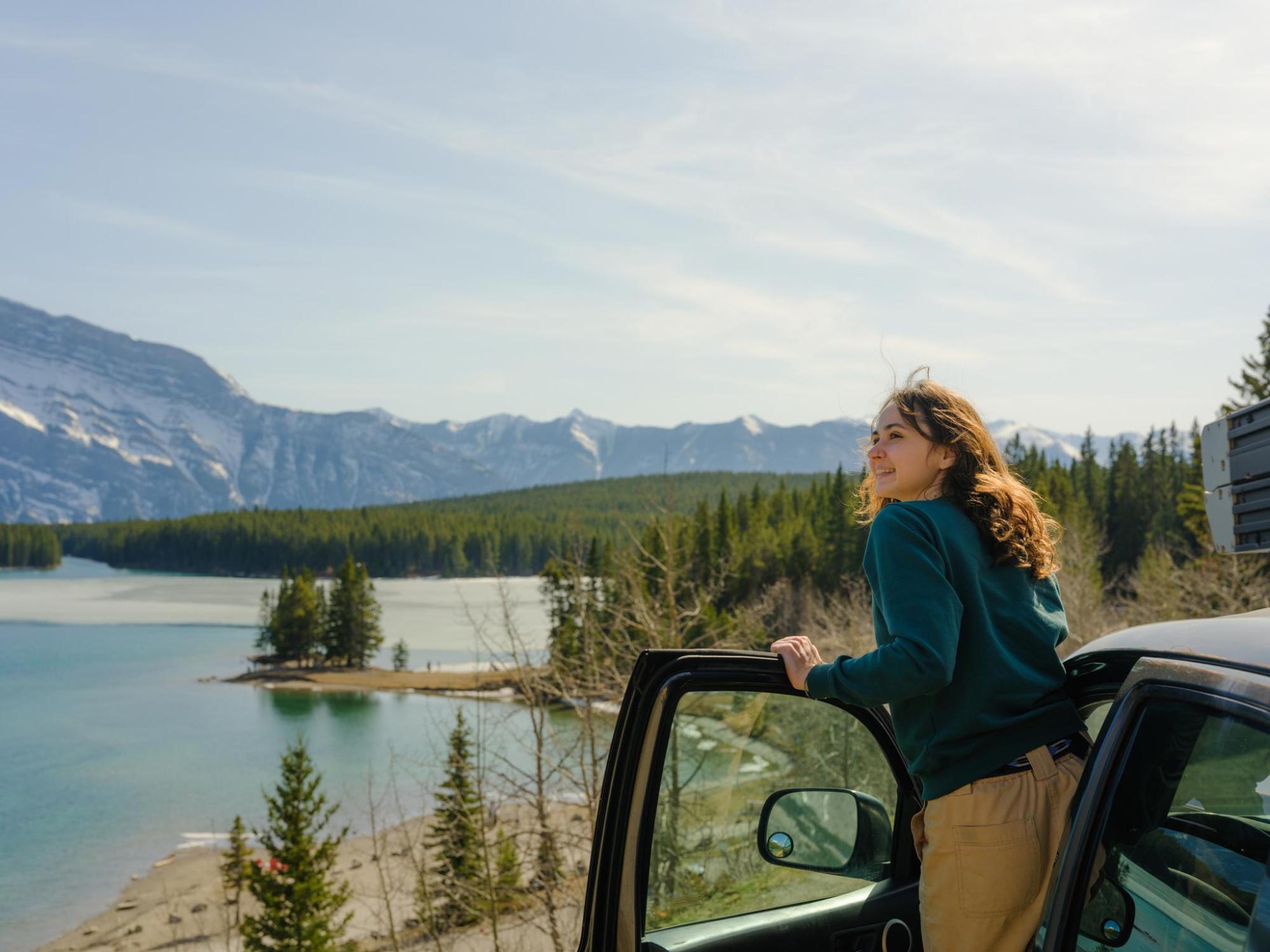 A woman gazes out a car window, with a scenic background.