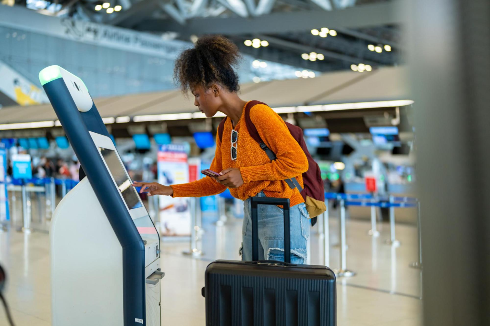 Passenger using airport self check-in kiosk with luggage
